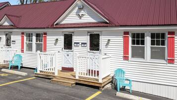 A row of white cabins with red shutters, numbered 10 and 9, and a wooden deck with chairs.