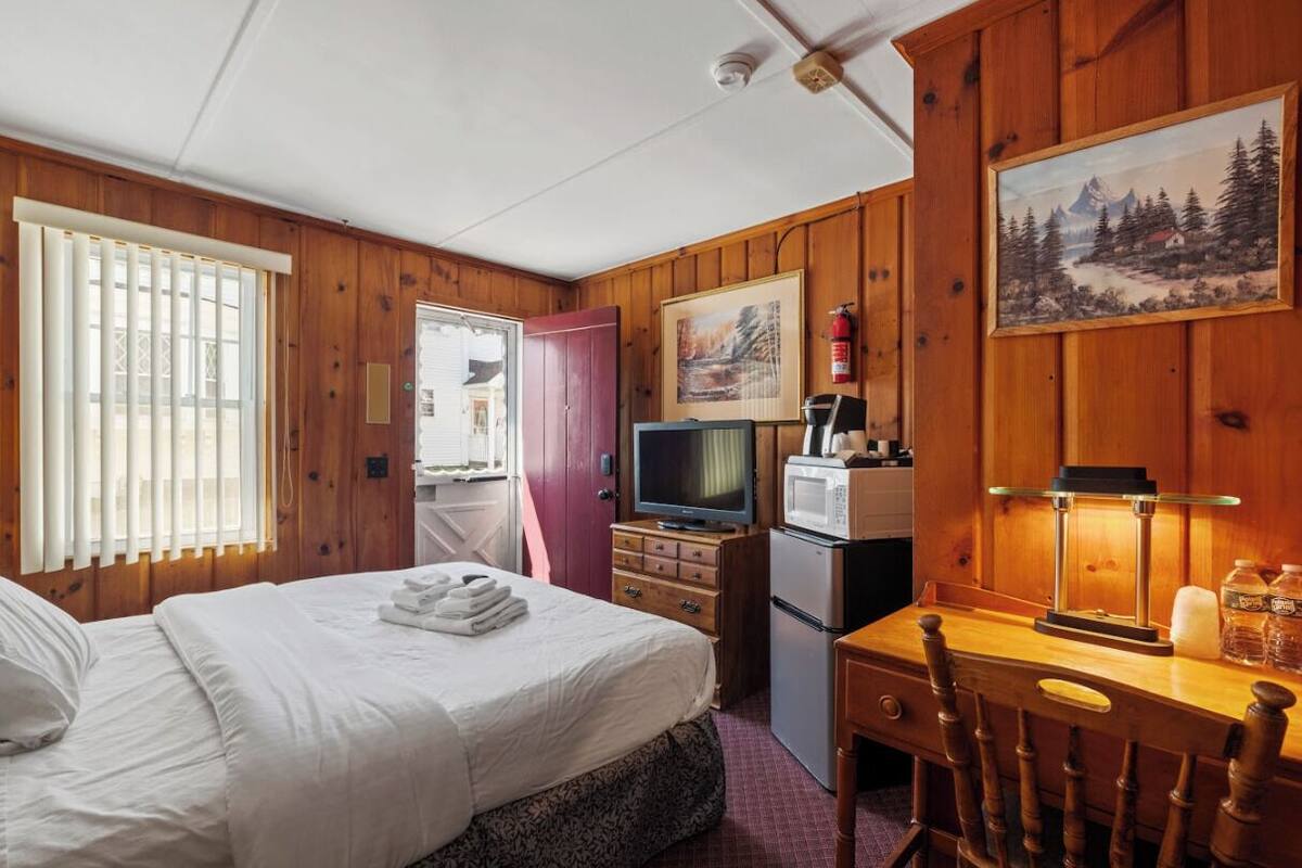 A room with a bed, a desk, a television, a microwave, and a painting on the wall.