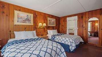 A room with wooden paneling, two beds with patterned bedding, wall-mounted lamps, and framed pictures.