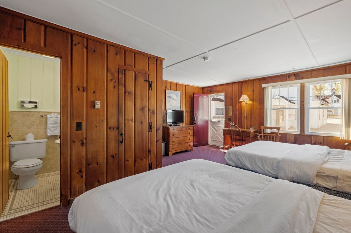 A room with wooden paneling, a bed, a dresser, a television, and a window with a view.