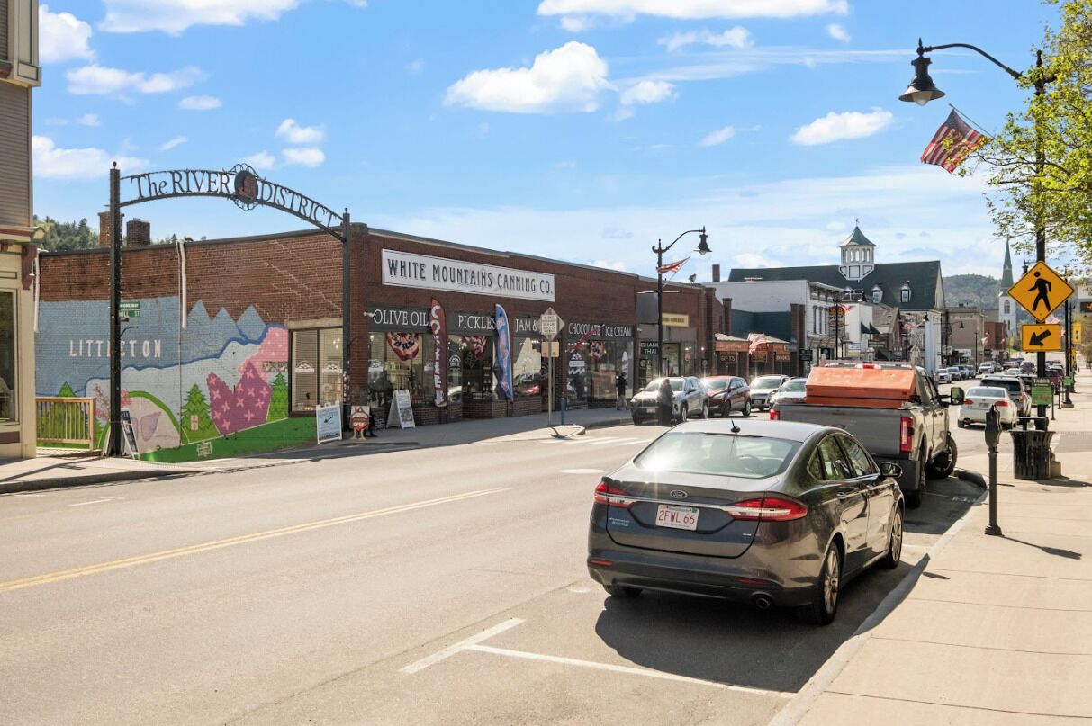 Una escena callejera con un edificio que muestra la leyenda 'The River District' y 'White Mountains Canning Co.'.