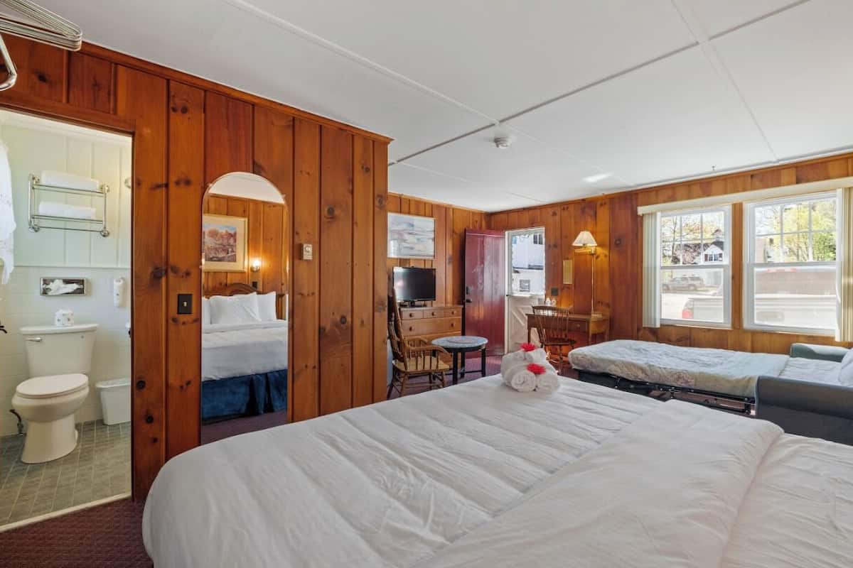 A hotel room with wooden paneling, a large bed, a desk, a chair, and a view through the window.