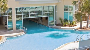 Una piscina con agua cristalina y azul, rodeada por un edificio con grandes ventanales.