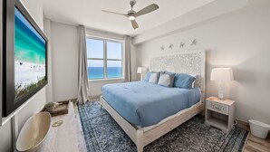 Un dormitorio con cama, ventilador de techo, televisión, ventana y mesita de noche.