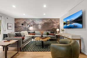 A modern living room with a sectional sofa, a coffee table, a leather armchair, a TV, and a wall mural.