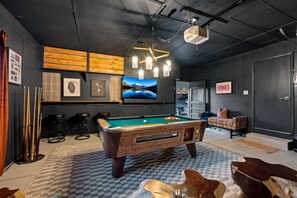 A pool table with a checkered floor, a mounted television, and a bar area with stools.