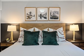 A hotel room with a large bed, two nightstands, three framed pictures on the wall, and two lamps.