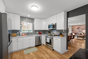 Une cuisine moderne avec des armoires blanches, des appareils en acier inoxydable et un plancher en bois.