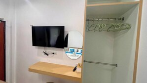 Habitación de hotel con televisión, espejo, toallero y estante de madera.