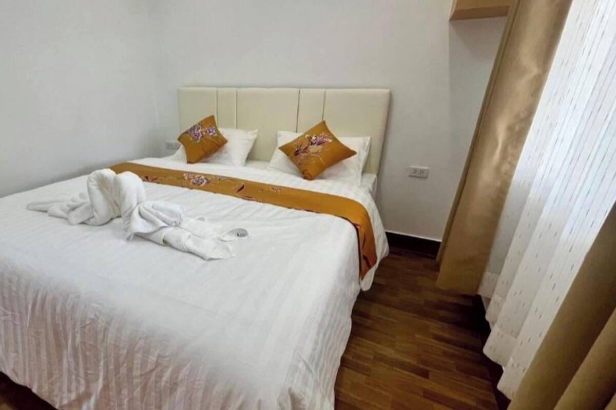 Une chambre d’hôtel avec un lit, du linge de lit blanc, un plancher en bois et une tête de lit blanche.