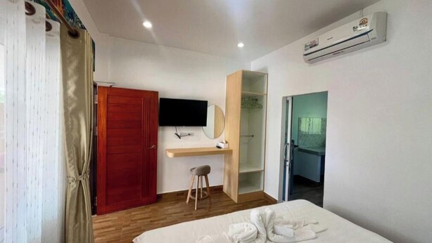 Una habitación de hotel con cama, escritorio, televisor, armario y unidad de aire acondicionado.