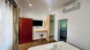 Una habitación de hotel con cama, escritorio, televisor, armario y unidad de aire acondicionado.