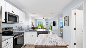 A modern kitchen with white cabinets, stainless steel appliances, a marble countertop, and a ceiling fan. - Beach Access 2BR @Grand Caribbean • Sleeps 6 • Views, Balcony & Pool (Orange Beach)