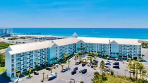 A multi-story hotel with a parking lot, surrounded by palm trees and a beach view. - Beach Access 2BR @Grand Caribbean • Sleeps 6 • Views, Balcony & Pool (Orange Beach)