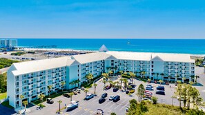 Ein mehrstöckiges Hotel mit Parkplatz, umgeben von Palmen und Blick auf den Strand.