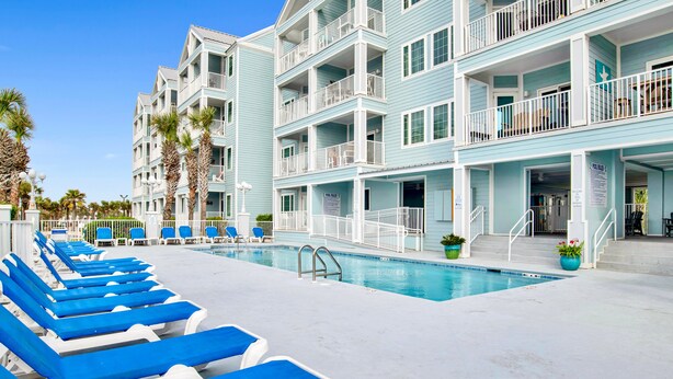 A hotel with a swimming pool, blue lounge chairs, and a light blue exterior. - Beach Access 2BR @Grand Caribbean • Sleeps 6 • Views, Balcony & Pool (Orange Beach)