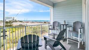 A balcony with Adirondack chairs, a small table, and a view of the beach and ocean. - Beach Access 2BR @Grand Caribbean • Sleeps 6 • Views, Balcony & Pool (Orange Beach)