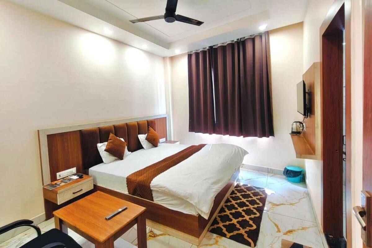 A hotel room with a bed, bedside table, chair, ceiling fan, window with curtains, and a TV.
