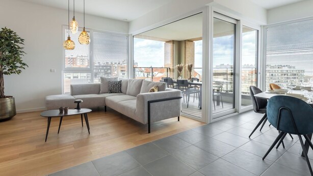 A modern living room with a sofa, coffee table, and dining area with chairs. - Beautiful apartment for 7 people with WIFI, TV and terrace (Blankenberge)