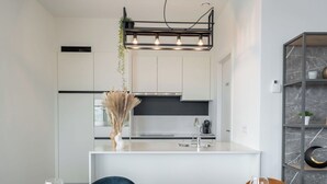 A modern kitchen with white cabinets, a marble countertop, and a hanging light fixture. - Beautiful apartment for 7 people with WIFI, TV and terrace (Blankenberge)