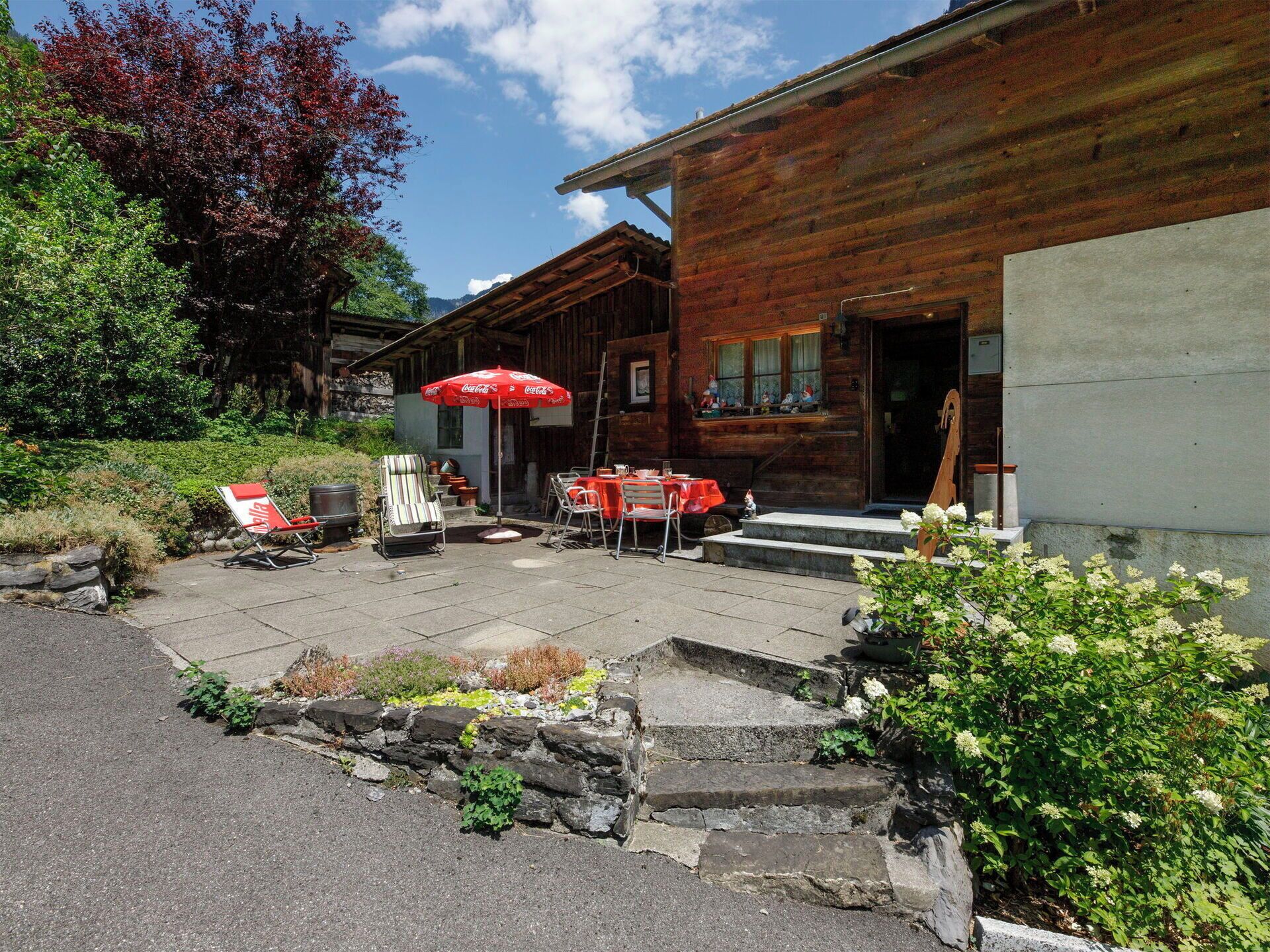 Un bâtiment en bois doté d’un patio comprenant des tables et des chaises, un espace extérieur aménagé pour s’asseoir et un parasol à l’effigie de Coca-Cola.