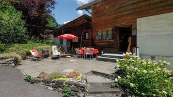 Un bâtiment en bois doté d’un patio comprenant des tables et des chaises, un espace extérieur aménagé pour s’asseoir et un parasol à l’effigie de Coca-Cola.