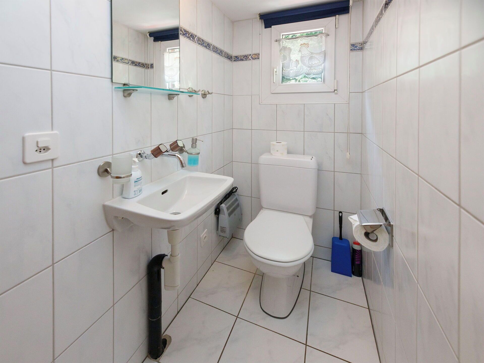Un baño pequeño con un lavamanos, inodoro y ventana con diseño decorativo.