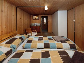 Quarto com duas camas, uma cômoda, uma cadeira e uma porta que dá para outro aposento.