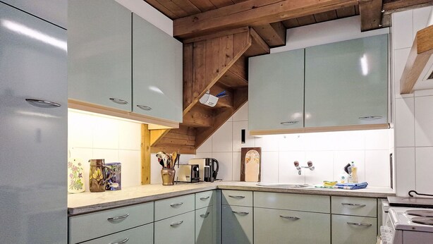 Cozinha com armários verde-claros, teto de madeira e painel de azulejos.
