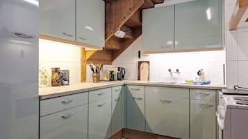 Une cuisine avec des meubles de couleur vert clair, un plafond en bois et un pare-feu en carrelage.