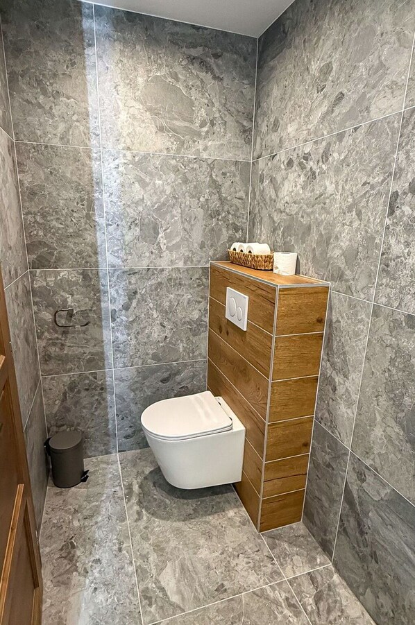 A bathroom with a white toilet, a wooden vanity, and a marble wall.