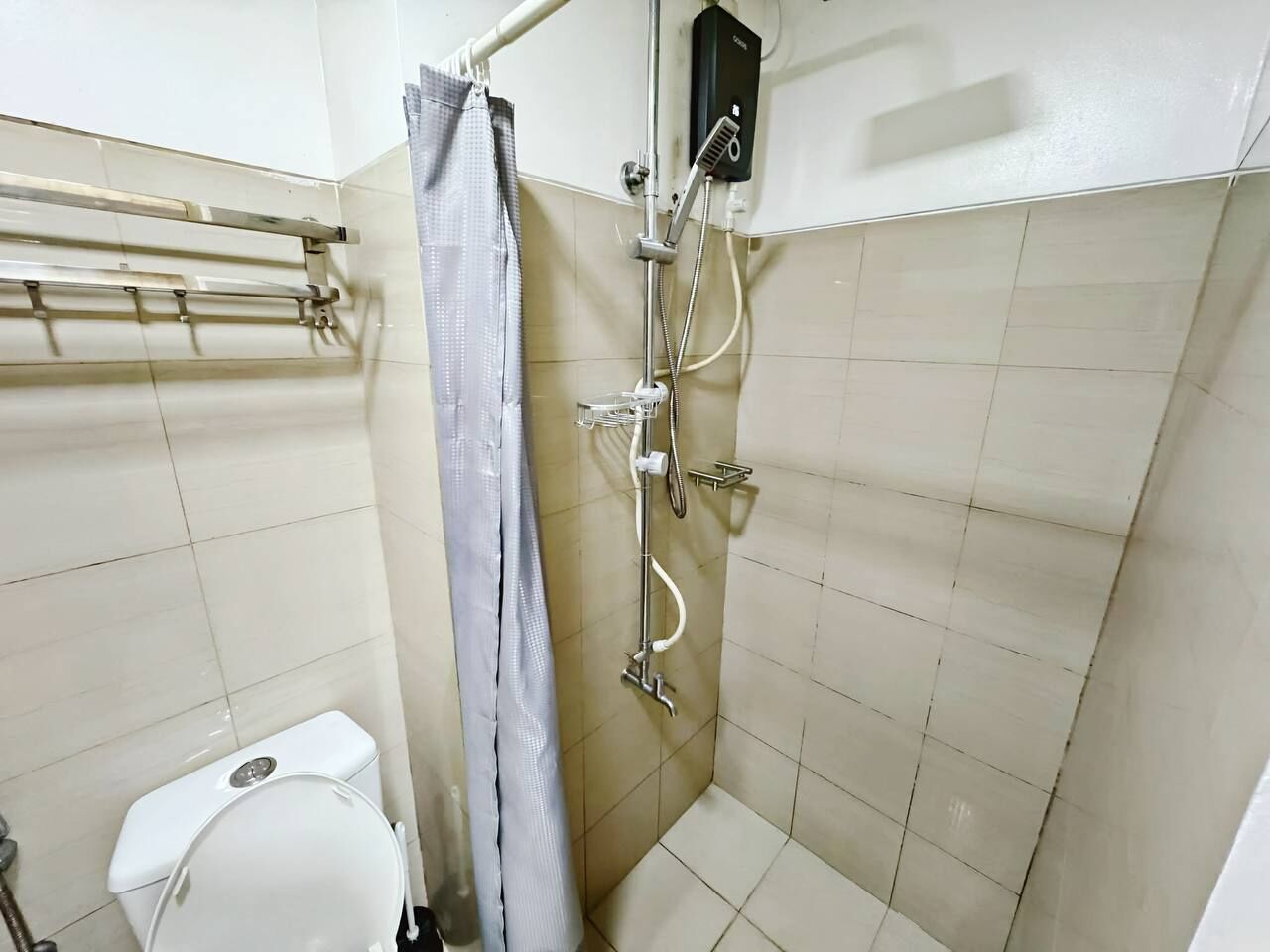 A small bathroom with a toilet, a shower with a handheld showerhead, and a towel rack.