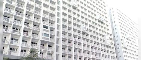 A high-rise building with multiple balconies, a sign for SMDC Shore, and a street with pedestrians and vehicles.