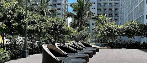 A row of outdoor lounge chairs in a courtyard with tall residential buildings in the background.