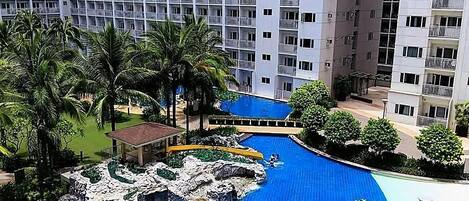 A high-rise hotel with a swimming pool, palm trees, and a rock feature.