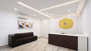 A reception area with a dark brown sofa, a reception desk, and a wall-mounted air conditioner. - Click Hotel Gachibowli Hyderabad (Hyderabad)