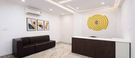 A reception area with a dark brown sofa, a reception desk, and a wall-mounted air conditioner.