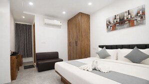 A modern hotel room with a large bed, a wooden wardrobe, a gray sofa, and a painting on the wall. - Click Hotel Gachibowli Hyderabad (Hyderabad)