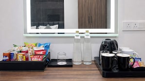 A hotel room with a minibar stocked with snacks, bottled water, and coffee mugs. - Click Hotel Gachibowli Hyderabad (Hyderabad)