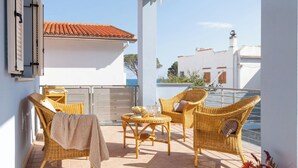 Un balcon agrémenté de meubles en osier, un bâtiment blanc surmonté d’un toit recouvert de tuiles rouges, et une vue dégagée sur la mer.