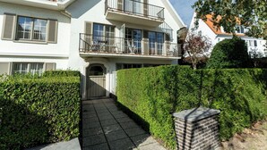 Un edificio residencial de dos plantas con un balcón, una entrada con reja y un seto bien cuidado.