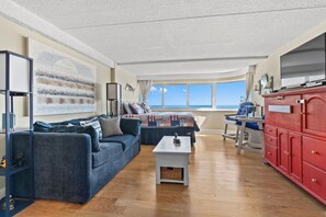 A living room with a sofa, a small table, a red cabinet, and a view of the ocean. - Atlantis Oceanfront Studio w Panoramic Views w pool and Free Linens (Ocean City)