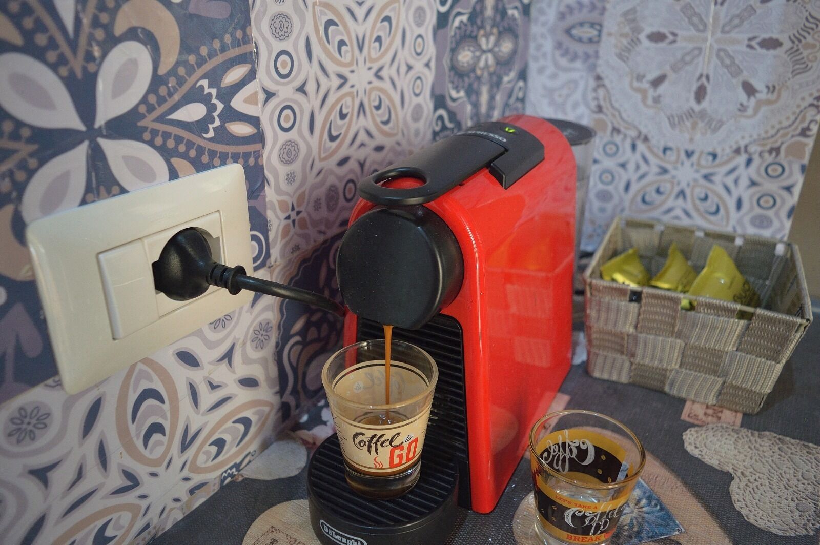 Eine Kaffeemaschine füllt Kaffee in eine Tasse, ein Glas Kaffee und ein Korb mit Kaffeekapseln.