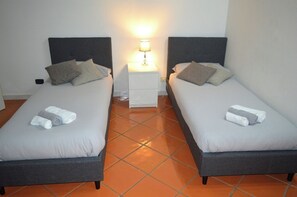 Une chambre avec deux lits, chacun équipé d’oreillers et de serviettes, une table de chevet avec une lampe et un sol carrelé.