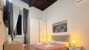 Un dormitorio con cama, mesitas de noche, escritorio, ventana con cortinas, radiador y una pintura de paisaje urbano en la pared.