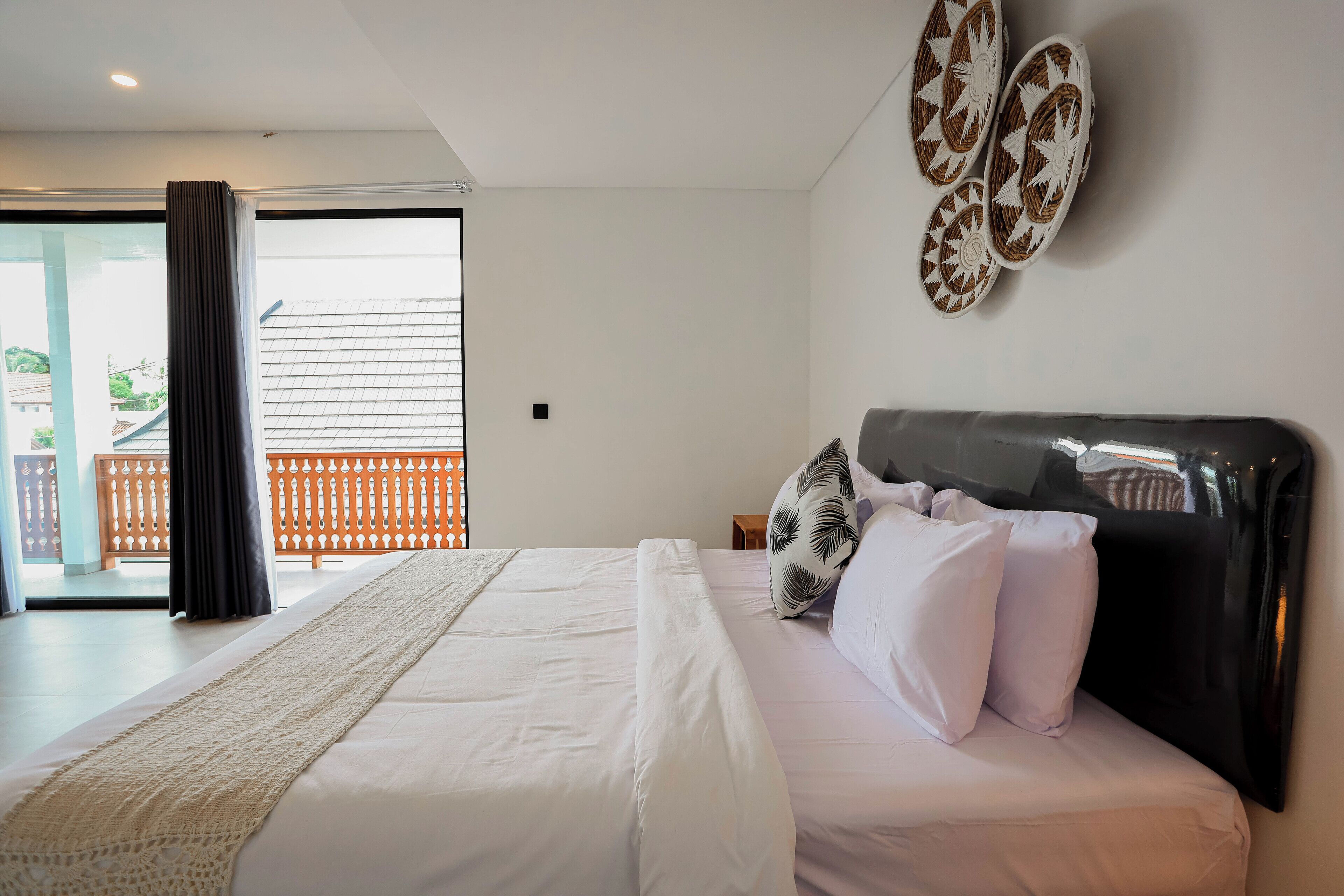 A bedroom with a bed, pillows, a headboard, a window with curtains, and a view of the outside.