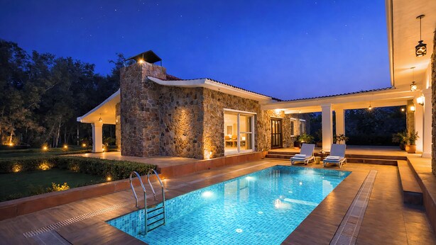 A swimming pool with a stone exterior and a covered patio area with lounge chairs. - ELIVAAS The Aravalli Reserve Isley Villa (Faridabad)