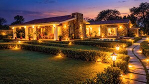 A stone building with a tiled roof, surrounded by well-manicured hedges and a paved pathway. - ELIVAAS The Aravalli Reserve Isley Villa (Faridabad)