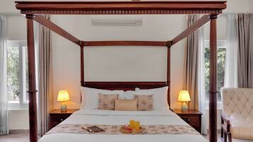 A four-poster bed with a wooden canopy, two bedside lamps, a tray with a book and a glass of juice, and a chair.