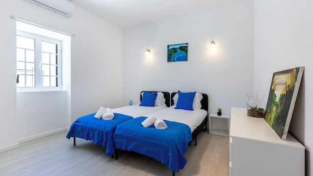 A hotel room with two beds, a window, an air conditioner, a painting, and a small plant on a nightstand. - Casa do Vale - in Paderne (Paderne)